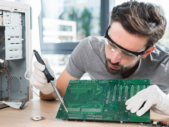 Un technicien répare une carte mère d'ordinateur, une étape essentielle dans le processus de reconditionnement visant à restaurer les appareils électroniques pour un usage fiable et durable.